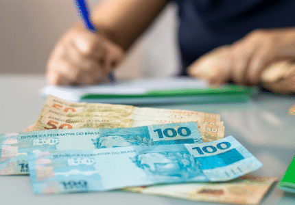 Pessoa montando seu fluxo de caixa e notas de cem reais e de cinquenta reais na mesa.