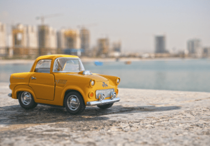 Miniatura de carro amarelo antigo em frente ao mar de uma cidade.