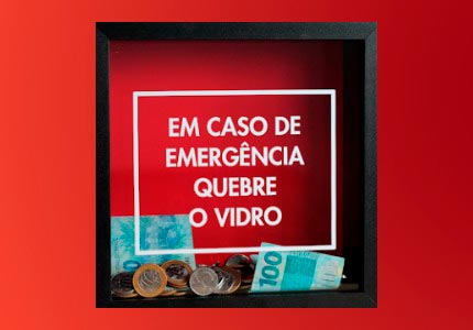 Quadro escrito no vidro Em caso de emergência quebre o vidro. Dentro do quadro notas de cem reais e moedas de um real.