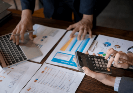 Duas pessoas fazendo cálculos na calculadora em uma mesa com várias folhas com gráficos.