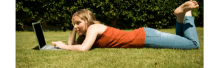Menina deitada na grama usando laptop para fazer cadastro no programa de fidelidade.