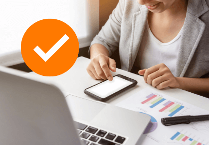 Mulher mexendo no celular com símbolo de check para empréstimo aprovado.