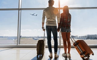 Casal em aeroporto com malas, prontos para viajar.