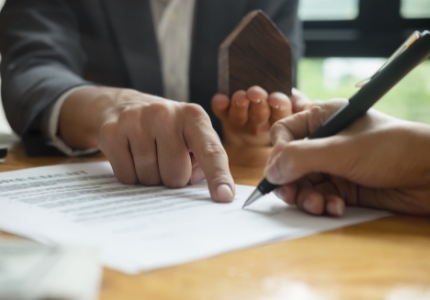 Uma mão assinando contrato aonde a mão de outra pessoa está indicando.