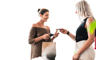 Mulher usando cartão de crédito para fazer um compra com outra mulher vendedora.
