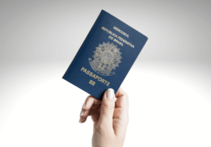 Mão segurando passaporte brasileiro.