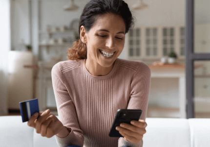 Mulher feliz com cartão de crédito em uma mão e celular no outro.