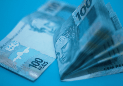 Várias notas de cem reais em um fundo azul representando um empréstimo para negativados.