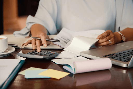 Pessoa fazendo cálculos para parcelamento da conta de luz atrasada. Mesa com papéis e uma calculadora.