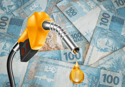 Pistola de combustível pingando óleo diesel, com notas de cinquenta de de cem reais ao fundo, representando o aumento do preço dos combustíveis.