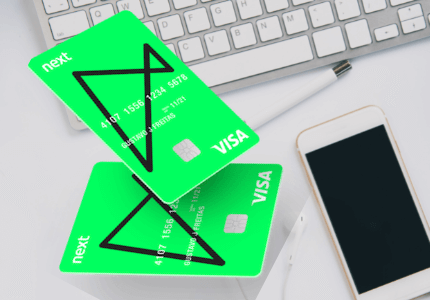 Dois cartões de crédito sem anuidade do Banco Next e em volta um celular e um teclado de computador.