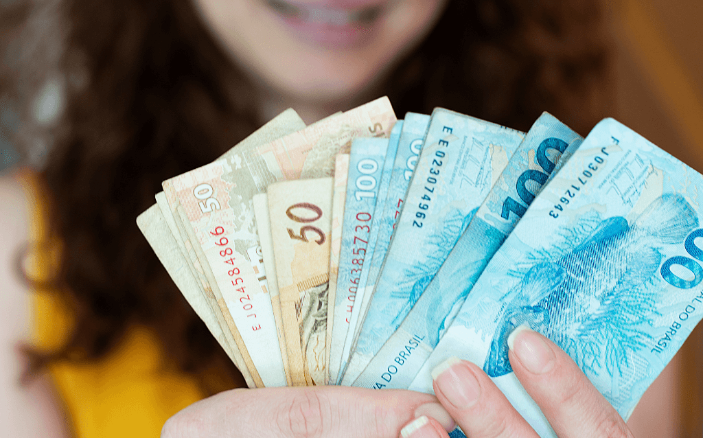 Mulher segurando notas de cem e cinquenta reais, indicando que pegou um empréstimo consignado pelo Auxílio Brasil.