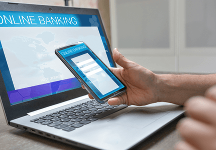 Laptop com internet banking na tela e aplicativo na tela do celular.