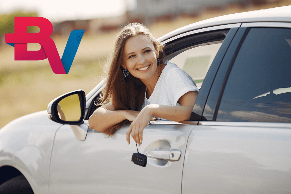 Mulher feliz no banco da frente de um carro, com o corpo posicionado para fora da janela , com a chave do veículo na mão, indicando ter pego o financiamento BV