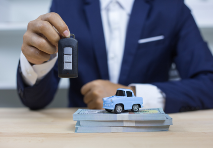 Homem segurando uma chave de carro, ao lado de um carro de brinquedo em cima de notas de dinheiro, simbolizando um financiamento de veículo Rodobens.