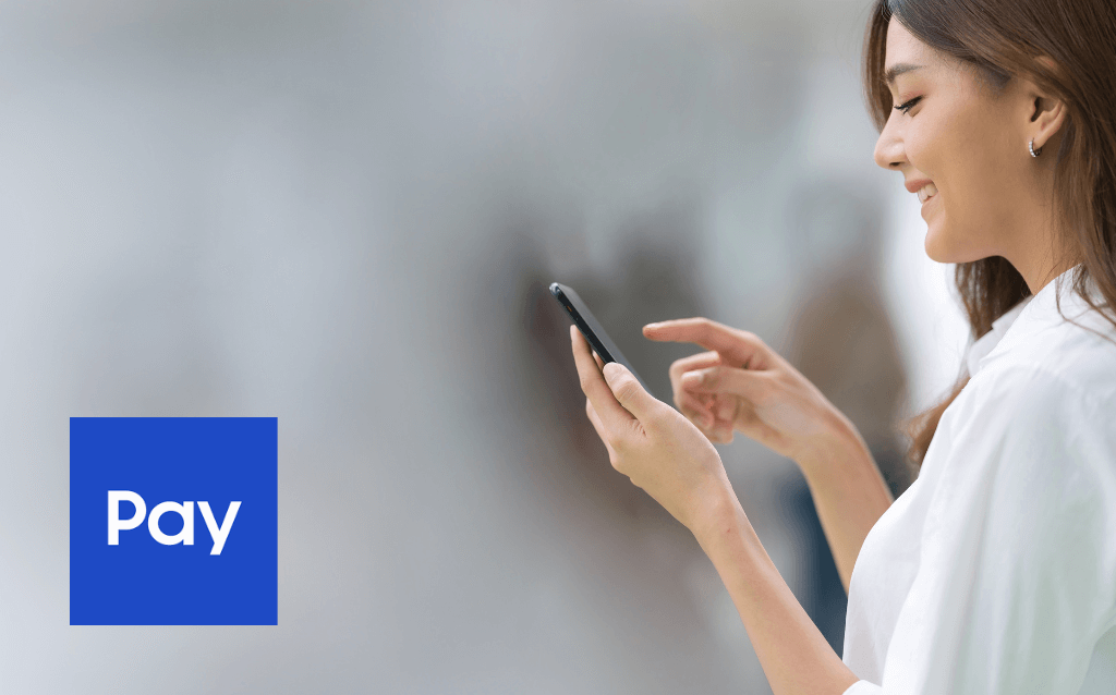 Mulher usando um smartphone para baixar o Samsung Pay e gerenciar seus cartões, com símbolo do app ao lado.