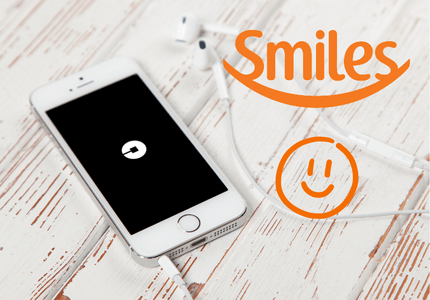Celular com o aplicativo da Uber aberto em tela, ao lado do símbolo da Smiles, representando a parceria entre a Uber e Smiles.