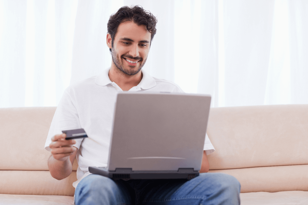 Homem com Notebook o colo e cartão de crédito na mão, comprando online.