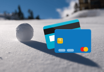Frente e verso de um cartão de crédito ao lado de uma bola de neve representando o problema que o rotativo pode trazer para o consumidor.