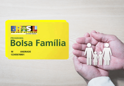 Cartão do Bolsa Família e ao lado duas mãos segurando uma família representada por bonecos de papel.