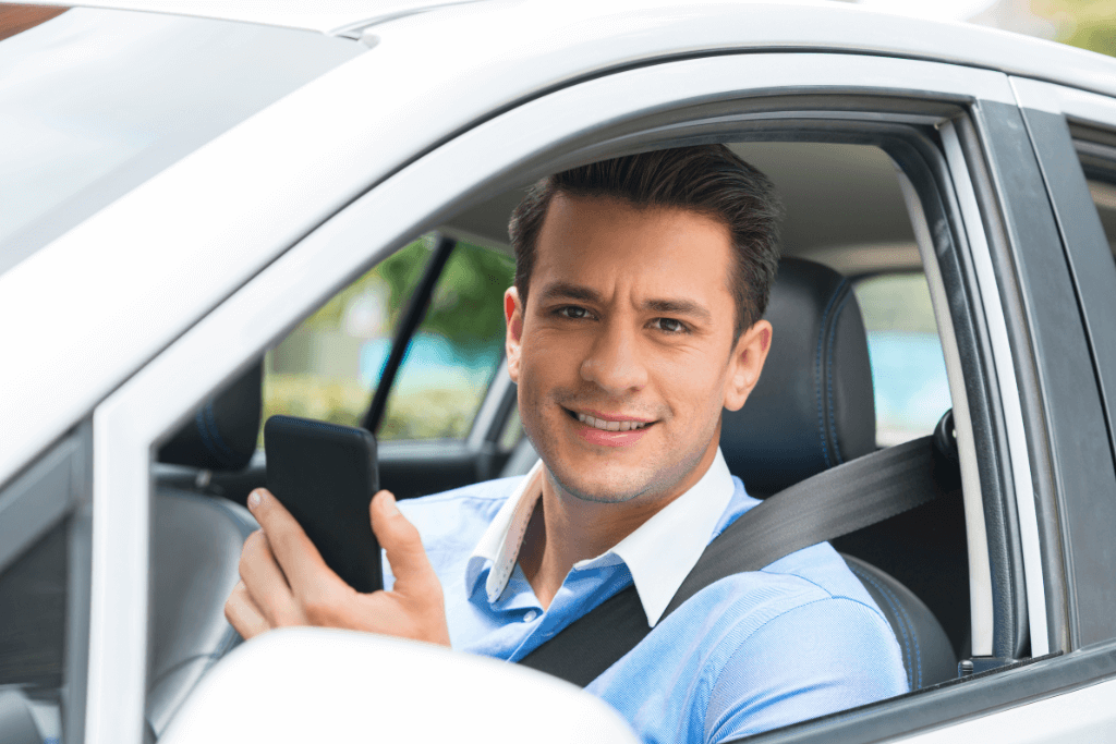 Motorista de aplicativo, sentado num carro, com um celular na mão.