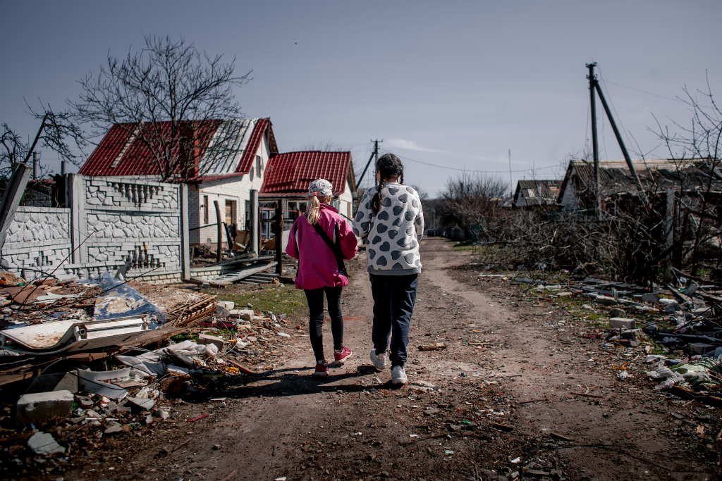 Pessoas andando num cenário devastado pela guerra entre Rússia e Ucrânia.
