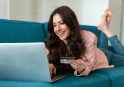 Mulher sorridente mexendo no laptop, deitada no sofá, representando a solicitação do cartão de crédito Bradesco Visa Platinum.