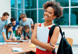Mulher, estudante, segurando materiais escolares e com uma mochila nas costas. Ela está feliz porque acabou de solicitar o cartão de crédito Santander SX Universitário.