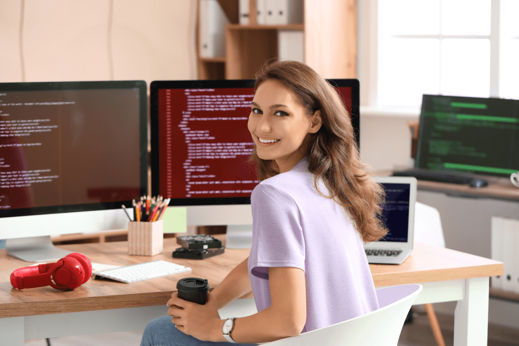 Mulher em frente a uma estação de computadores, com um café na mão.