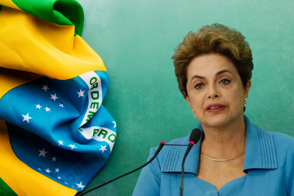 Dilma Rousseff discursando ao lado da bandeira do Brasil.