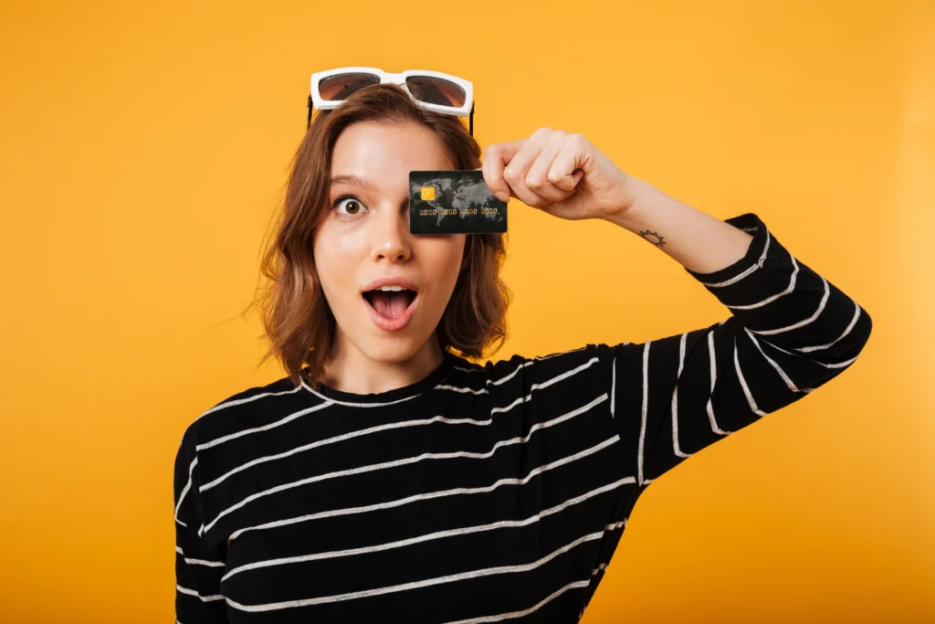 Jovem mulher segurando cartão de crédito próximo ao rosto.