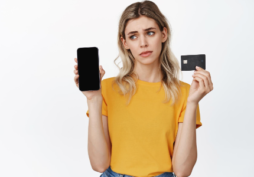 Mujer confundida con tarjeta de crédito y celular tras rechazo de solicitud bancaria
