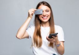 Mulher sorrindo segurando cartão de crédito e celular, representando uso consciente do cartão e controle financeiro