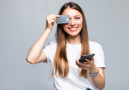 Mulher sorrindo segurando cartão de crédito e celular, representando uso consciente do cartão e controle financeiro
