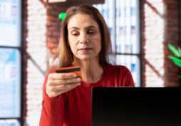 Mulher analisando cartão de crédito enquanto usa notebook, representando aumento de anuidade e cobrança na fatura