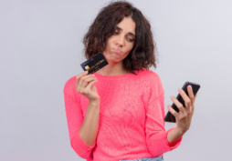 Mulher com expressão de preocupação segurando cartão de crédito e celular, representando dívida por anuidade e risco de negativação