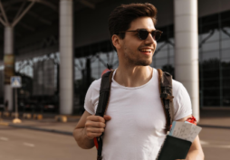 Homem com passaporte e mochila em aeroporto, representando uso de conta multimoeda e viagens internacionais